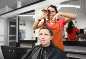 Portrait of hairdresser going to cut lock of long hair with scissors tool, female client scared in masters chair. Beauty salon, barbershop, image concept