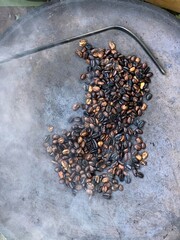 coffee beans being roasted by hand in the traditional way on a wood-fired stove seen from above through the smoke