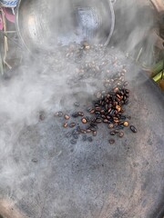 coffee beans being roasted by hand in the traditional way on a wood-fired stove seen from above through the smoke