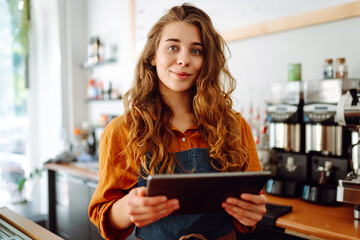 Smiling female barista takes an order from a panchette while standing at the bar counter in a...