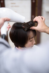 女性の髪をヘアスタイリングする美容師の手元のクローズアップ