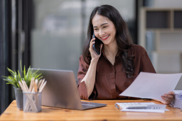 Fototapeta na wymiar Cheerful business Asian woman freelancer making telephone call share good news about project working in office workplace, business finance concept. 