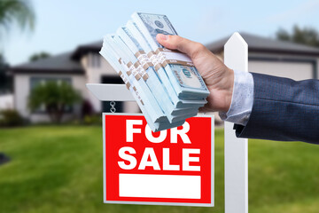 Buyer Handing Over Cash for House with Home and For Sale Real Estate Sign Behind.