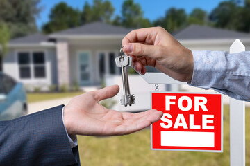 Real Estate Agent Handing Over the House Keys in Front of a Beautiful New Home and For Sale Real Estate Sign.