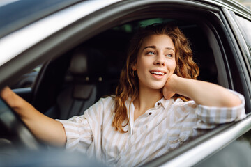 Cute woman in casual clothes is sitting behind the wheel of a car. Traveler-driver. Concept of mode...