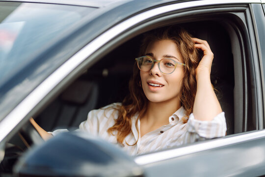 Cute woman in casual clothes is sitting behind the wheel of a car. Traveler-driver. Concept of mode of transportation, travel.