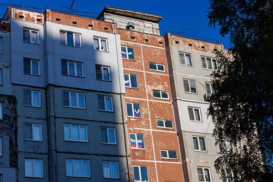 typical russian ugly high rise apartmant building with russian national flags in some windows at summer day.
