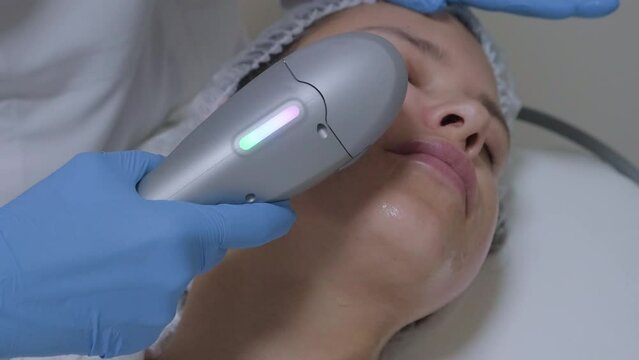 Hardware ultrasound cosmetic procedure in a beauty clinic. Skin rejuvenation, smas lifting anti-age therapy. Close-up beautician hands work with female patient face skin.