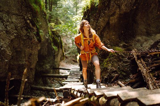 Happy woman in hiking clothes with a yellow backpack walks along a wooden hiking path in the mountains. Hiking, active lifestyle. Outdoor adventure concept.