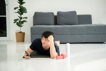 Lazy man with dumbbell and smartphone on yoga mat