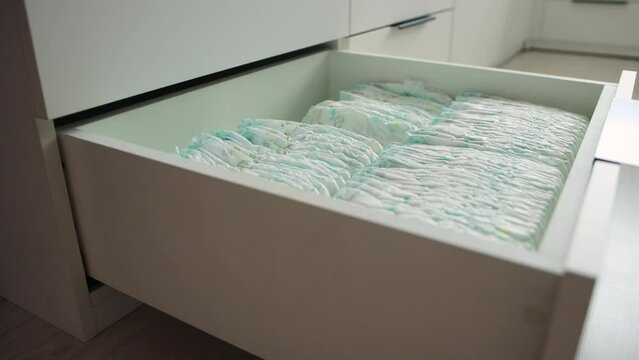 The man opened the chest of drawers with baby diapers, took the diapers and closed the chest of drawers. Cotsnept protection against leakage of children, hypoallergenic diapers, hygiene. Close-up