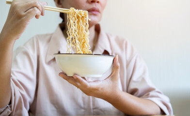Woman using chopsticks eating instant ramen, noodles, cheap food and no money for dinner