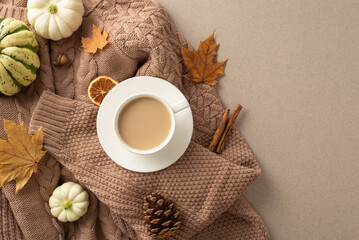 Autumn's charm. Top view shot: brown sweater, coffee mug on saucer, raw pattypans, acorn, cinnamon...