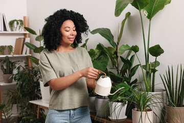 Happy woman watering beautiful potted houseplants at home