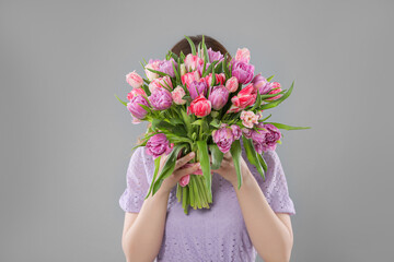 Woman covering her face with bouquet of beautiful tulips on grey background