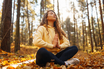 Young woman performs yoga exercises in the autumn forest, on fallen leaves. Lifestyle, meditation concept. Enjoying.