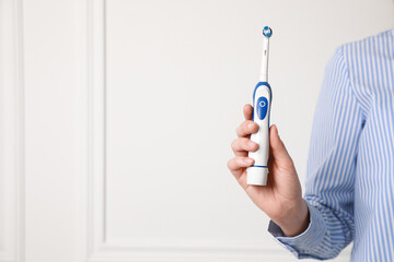 Woman holding electric toothbrush near white wall, closeup. Space for text