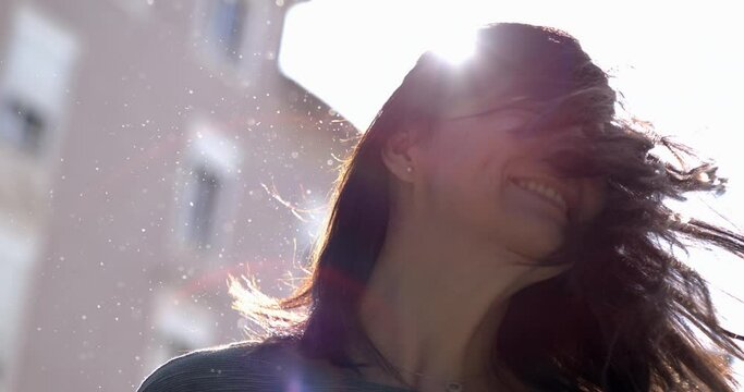 Carefree woman shaking hair in super slow-motion outside in the sunlight with flare. 800 fps clip of 30s adult girl shakes head sideways