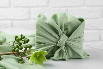 Furoshiki technique. Gift packed in green fabric and plants for decor on white table
