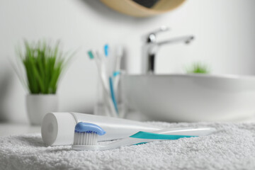Plastic toothbrush with paste and tube on white towel in bathroom, closeup. Space for text