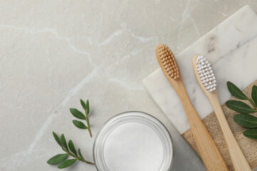 Bamboo toothbrushes, glass bowl of baking soda and green leaves on light grey marble table, flat...