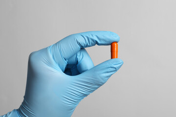 Doctor holding pill on grey background, closeup