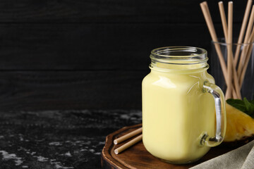 Tasty pineapple smoothie, slice of fruit and straws on dark textured table. Space for text