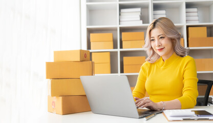 Beautiful young Asian woman working with online sales box with laptop taking online orders at home, SME business concept