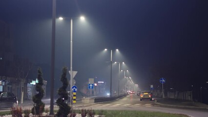 Traffic on foggy misty night road illuminated by street lights