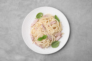 Plate of tasty pasta Carbonara with basil leaves on grey table, top view