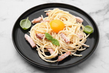 Plate of tasty pasta Carbonara with basil leaves on white marble table