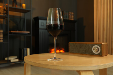 Glass of red wine and portable bluetooth speaker on table in room. Relax at home