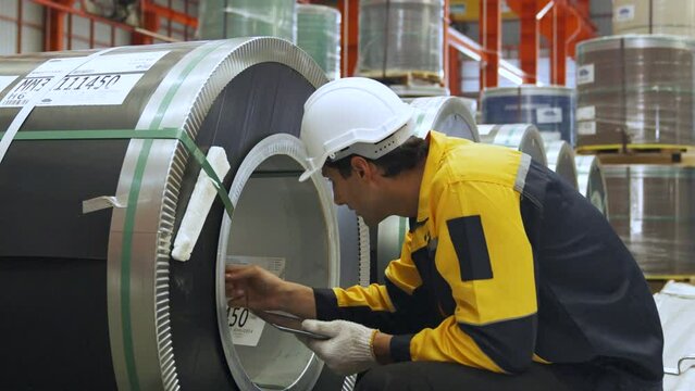 Male engineer in professional industrial factory,Workers wear safety helmets and carry checklist documents,Production experts walk around to inspect the readiness of steel sheet roll materials.
