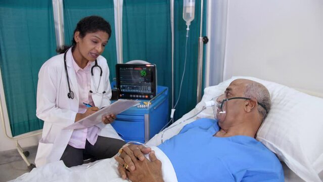 A female healthcare worker with her elderly patient - checking ecg monitor  heart monitor  medical diagnosis . An elderly Indian patient is breathing through an oxygen mask while lying on the bed -...