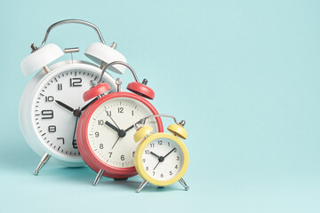 Three alarm clocks of different colors and sizes on a blue background.