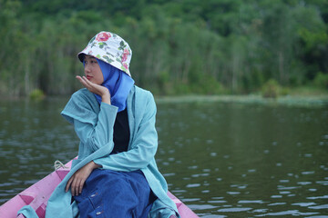 a beautiful Muslim girl posing wearing a hat with a floral motif and a blue blazer on a canoe in a beautiful lake