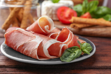 Rolled slices of delicious jamon and basil on wooden table, closeup