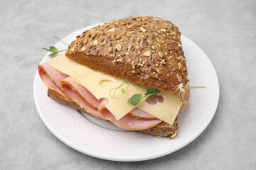 Delicious sandwich with ham and cheese on light gray table, closeup