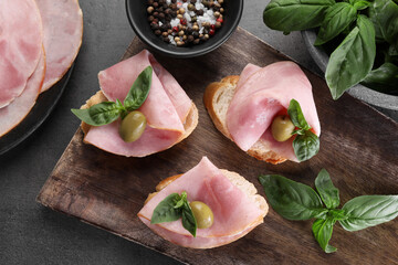 Delicious sandwiches with ham, basil, olives and spices on grey table, flat lay