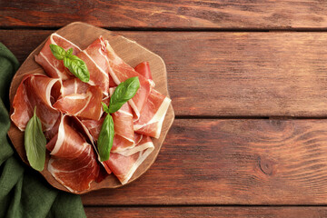 Slices of tasty cured ham and basil on wooden table, top view. Space for text