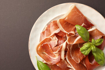 Slices of tasty cured ham and basil on grey background, top view. Space for text
