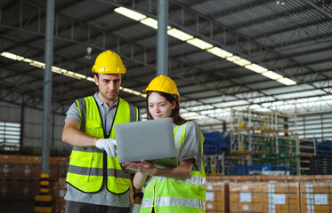 Female engineer in helmet and safety vest holding latop discussing with male engineer in factory.