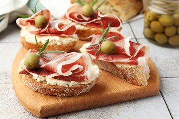 Tasty sandwiches with cured ham, rosemary and olives on tiled table, closeup