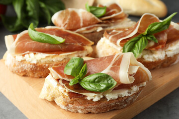 Tasty sandwiches with cured ham and basil on wooden board, closeup