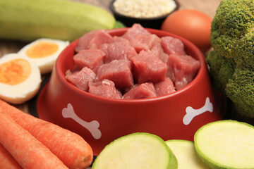 Raw meat in bowl and healthy products for pet on table, closeup