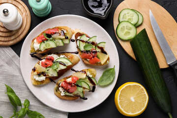 Delicious bruschettas with balsamic vinegar, toppings and products on dark textured table, flat lay
