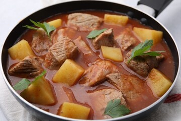 Delicious goulash in saucepan on table, closeup