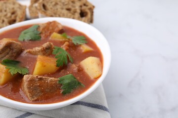 Delicious goulash in bowl on white table, closeup. Space for text