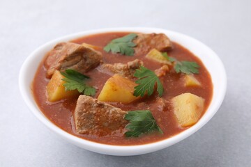 Delicious goulash in bowl on light grey table, closeup