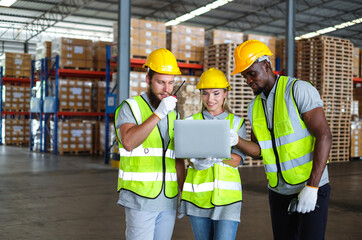 Female industrial engineer holding laptop discussing with two male factory engineers about storage management in warehouse.